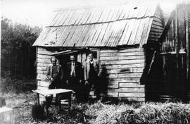 View of three men standing outside a rough hewn timber building in the bush. Macquarie Harbour, T...